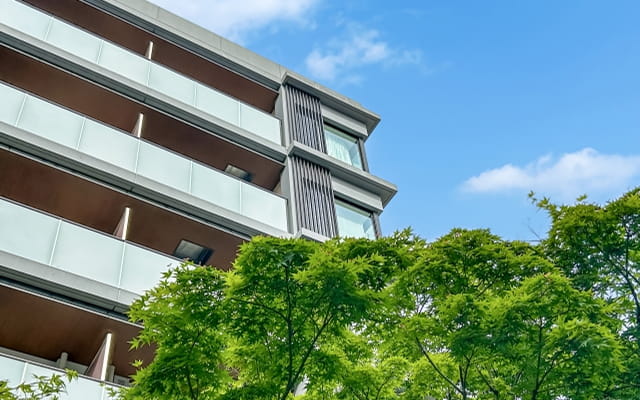 青空の下に立つ現代的な建物と、手前に広がる緑の木々