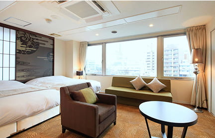 ベッドと円形テーブル、ソファが整然と並ぶ、シンプルで清潔感のあるホテルの一室