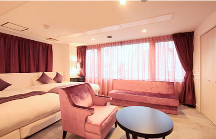 赤いカーテンと照明が温かみを演出する、ベッドとソファが配置された落ち着いた客室