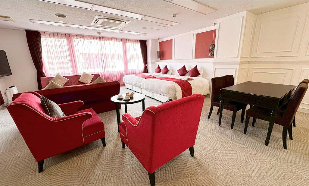 赤いソファとチェアが印象的な広々とした客室で、ベッドとダイニングテーブルも備えられている