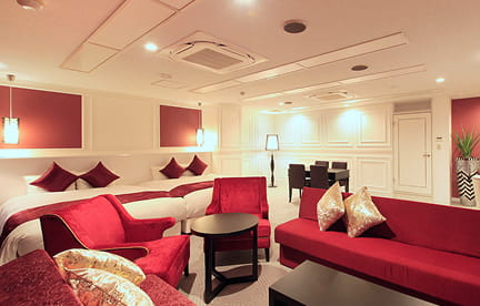 赤いクッションとソファがアクセントになった、暖かみのあるホテルの客室空間