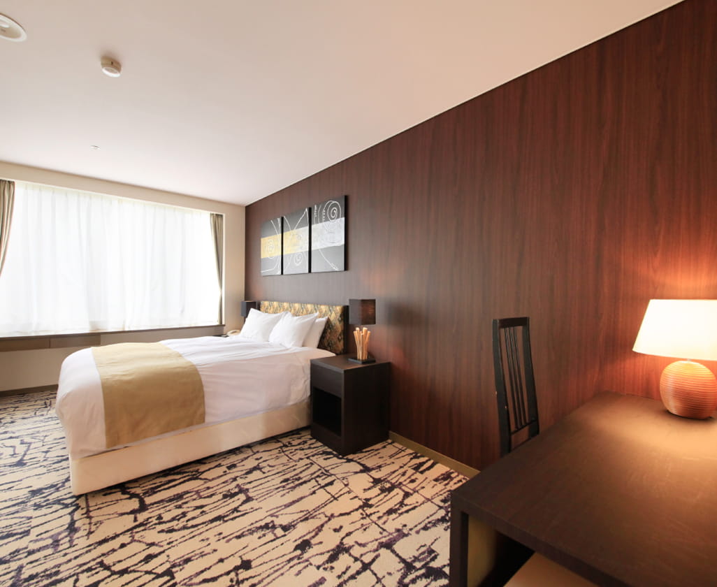 大きな窓から光が差し込む明るい室内で、木目調の壁がアクセントのスタイリッシュな客室
